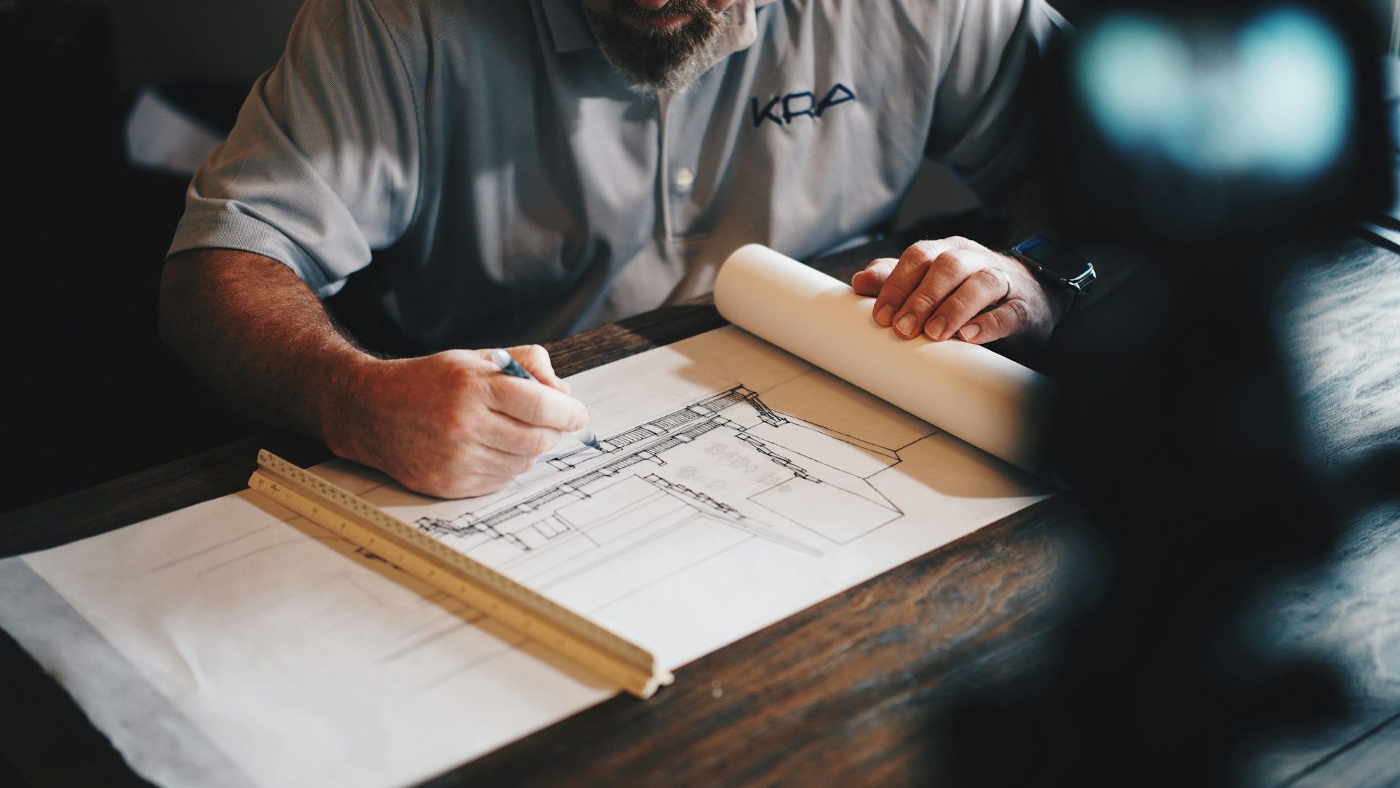 Sangeetha drafting a house elevation by hand with a pencil and ruler.